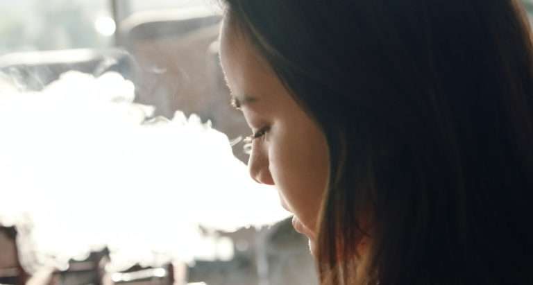 young girl with brown hair and smoke coming out of her mouth, side profile
