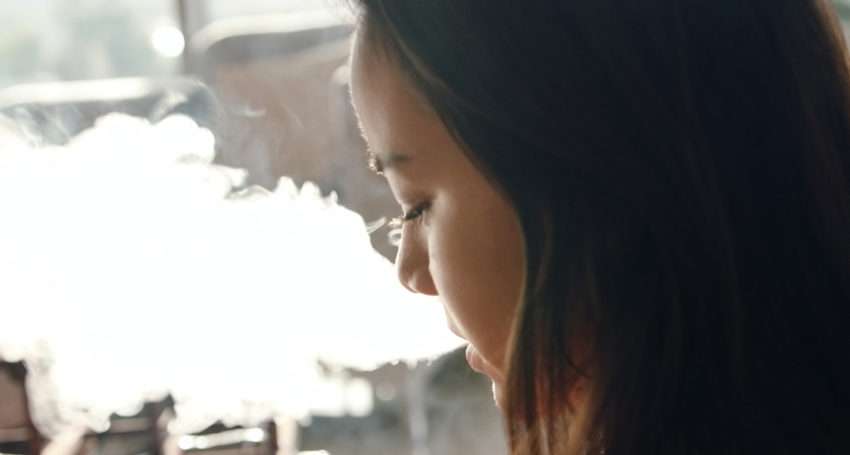 young girl with brown hair and smoke coming out of her mouth, side profile