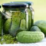 A close up of a glass jar full of pickles. A few cucumbers lay outside the jar waiting to be brined.