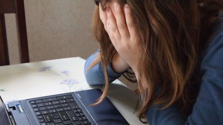woman with hands over face in distress looking at laptop