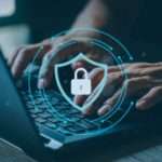 two hands typing on a laptop with a blue circle layered over. The circle has a lock and a shield inside it.