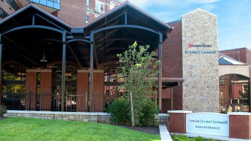 a brown hospital bulding with a green yard. a sign says montefiore st. luke's cornwall